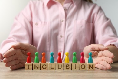 Woman protecting colorful pawns and wooden cubes with word Inclusion at table, closeup