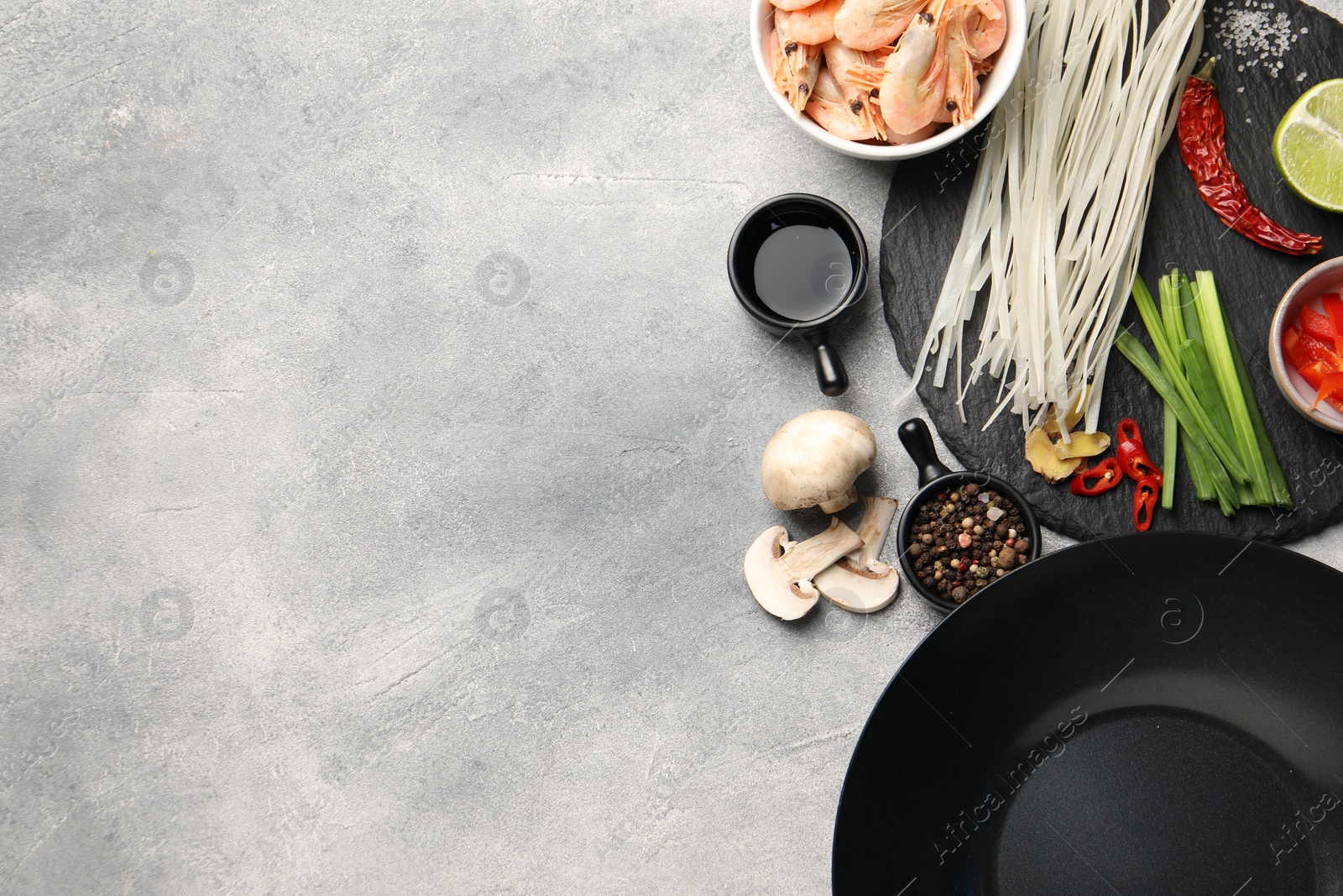 Photo of Flat lay composition with black wok, spices and products on grey textured table. Space for text