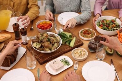 Photo of Friends eating vegetarian food at wooden table indoors, closeup