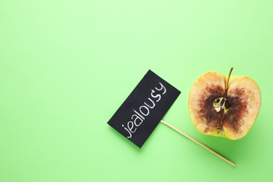 Photo of Rotten apple and JEALOUSY sign on green background, flat lay. Space for text