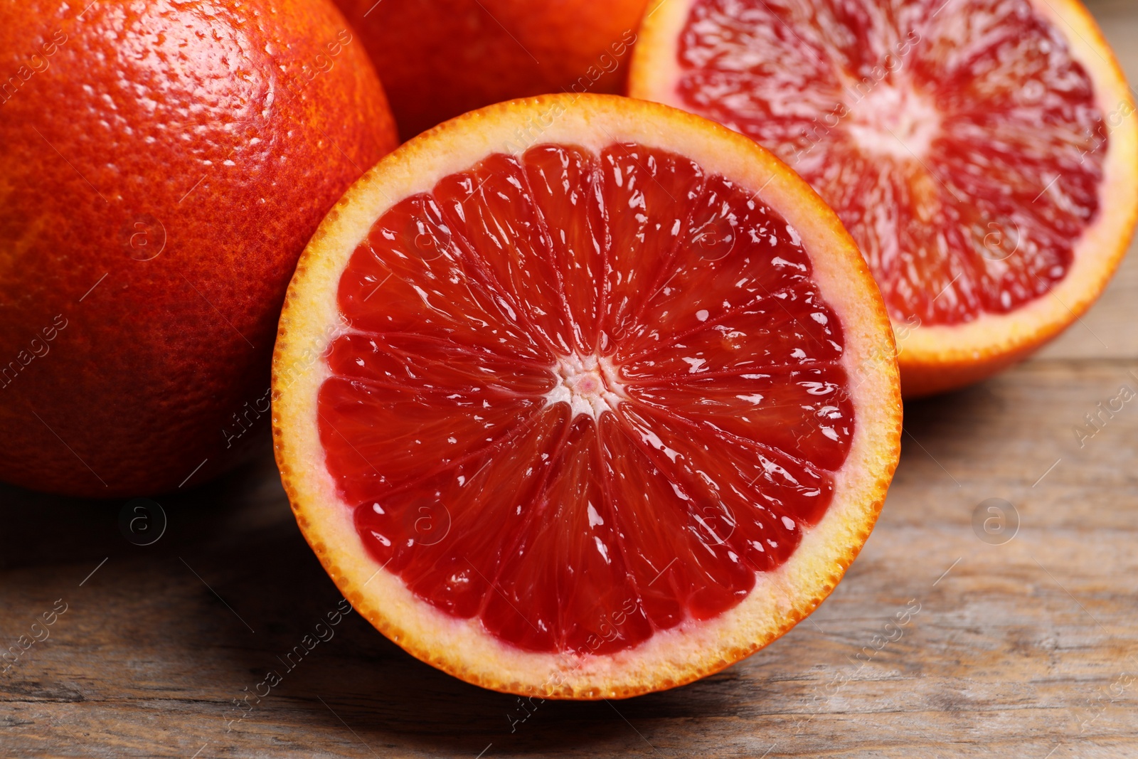 Photo of Whole and cut red oranges on wooden table, closeup