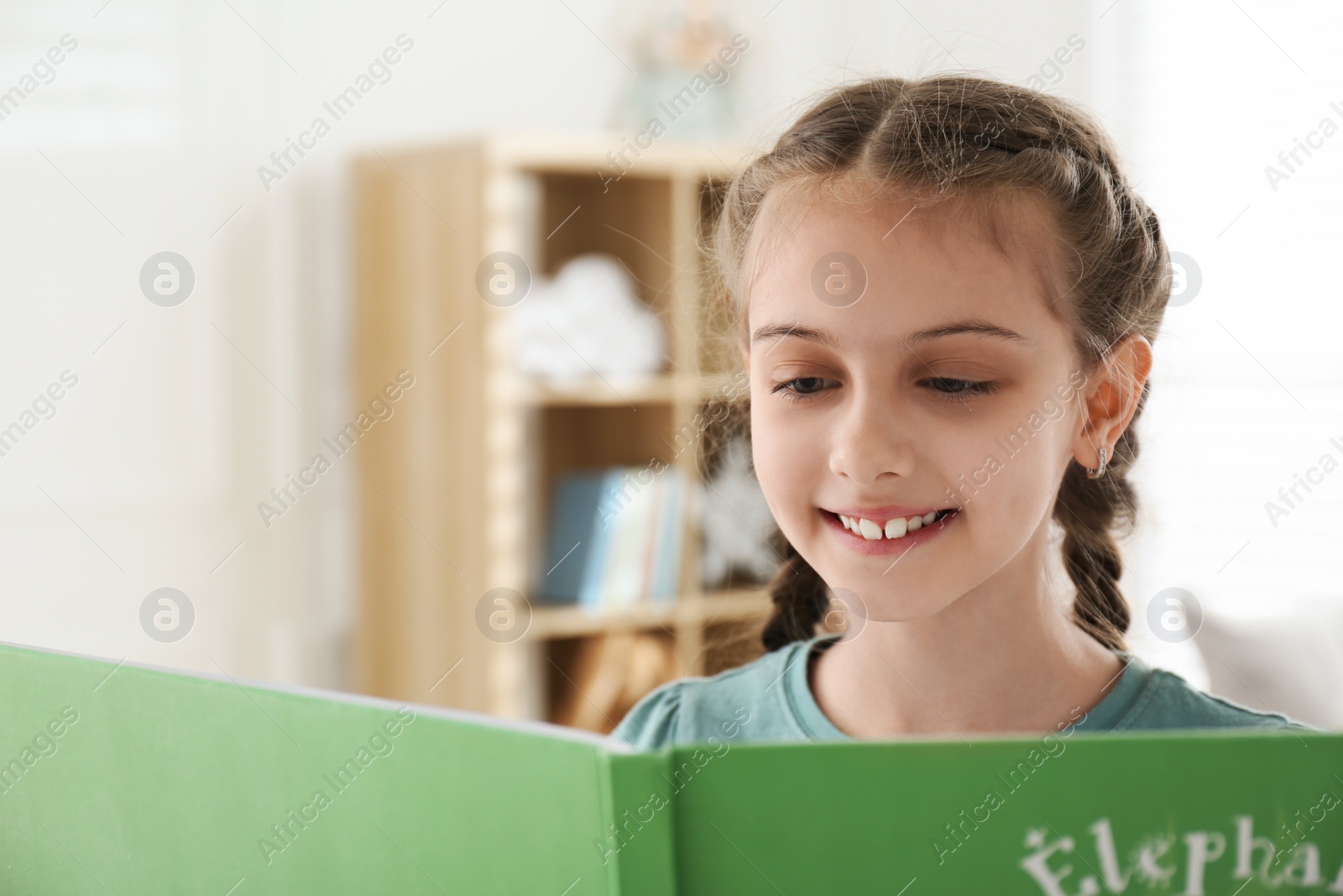 Photo of Cute little girl reading book at home