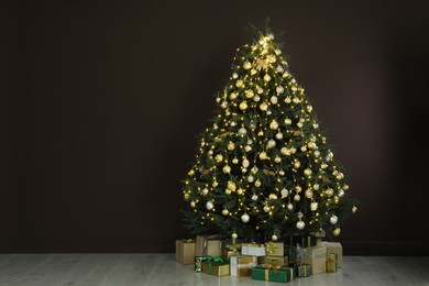 Photo of Beautifully decorated Christmas tree and many gift boxes near brown wall indoors, space for text