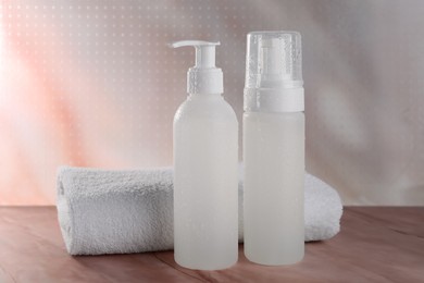 Photo of Bottles with face cleansing products and towel on beige marble table