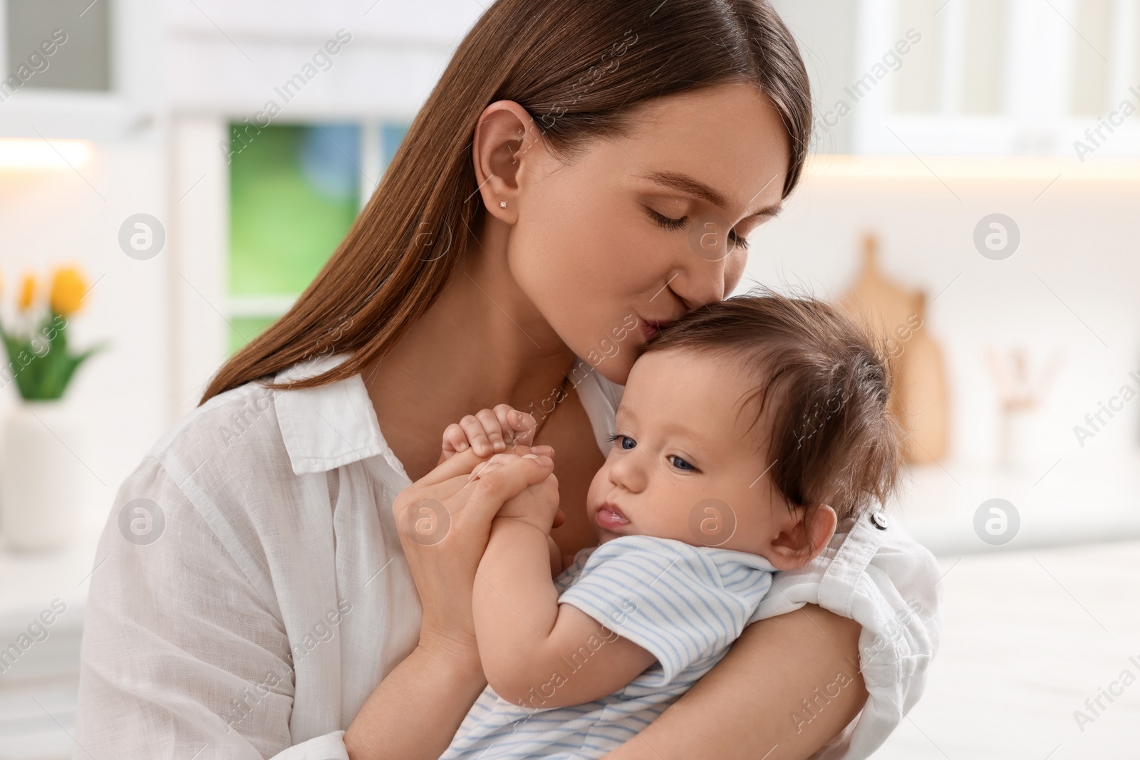 Photo of Happy mother kissing her little baby in kitchen