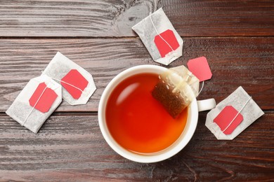 Photo of Tea bags and cup of hot beverage on wooden table, flat lay