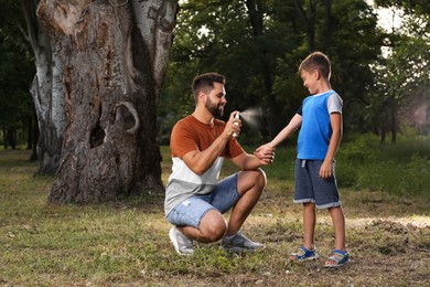 Photo of Man applying insect repellent on his son's leg in park. Tick bites prevention