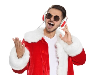 Young man in Santa costume listening to Christmas music on white background