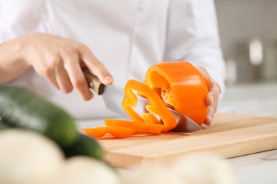 Photo of Professional chef cutting cut bell pepper at white marble table in kitchen, closeup