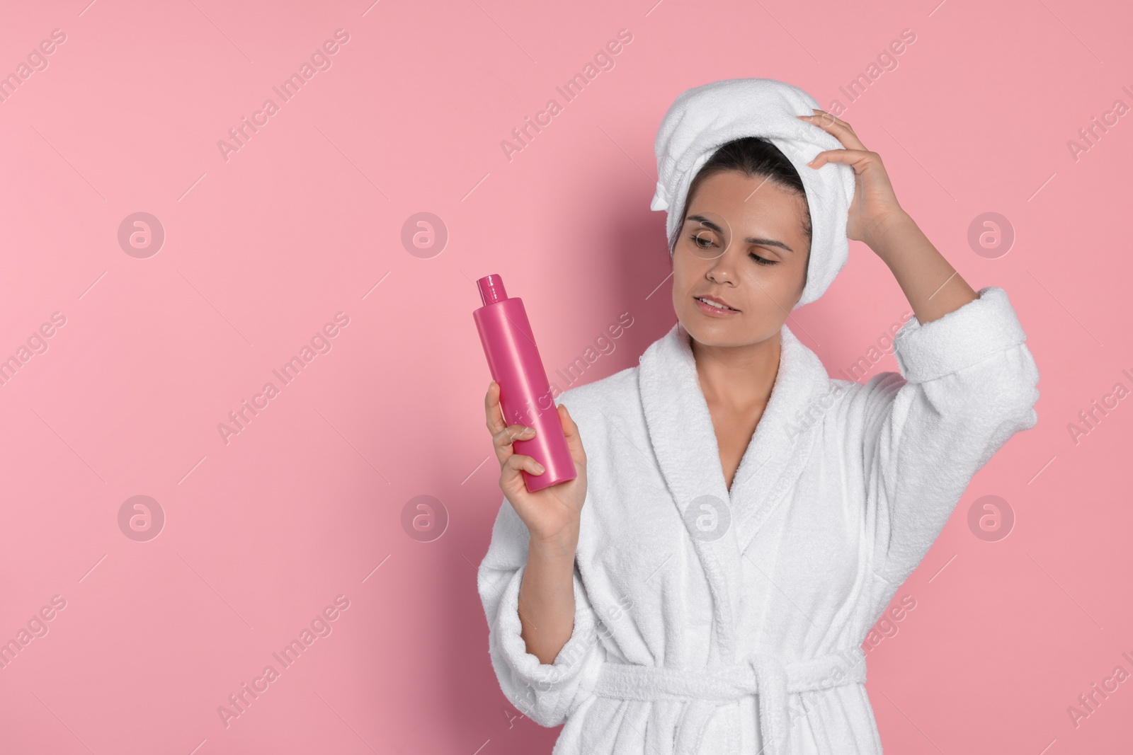 Photo of Beautiful young woman holding bottle of shampoo on pink background, space for text