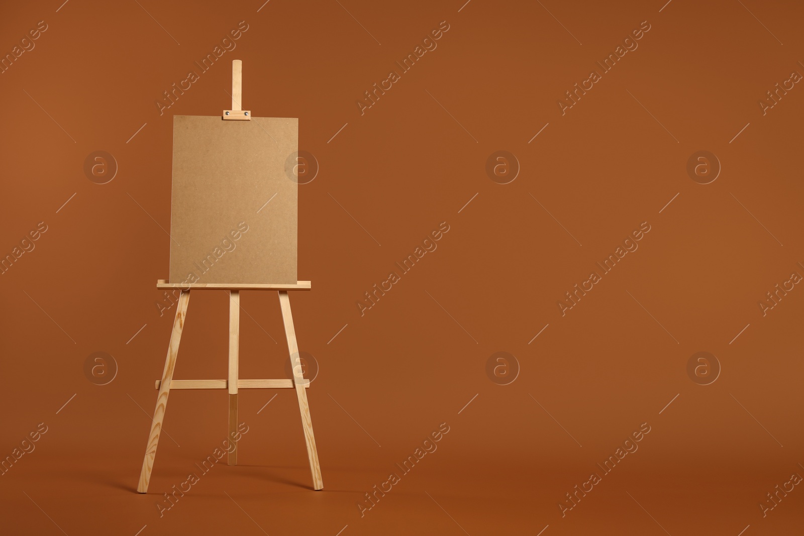 Photo of Wooden easel with blank board on brown background. Space for text