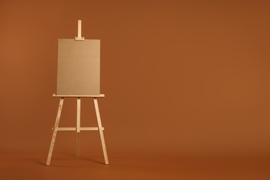 Photo of Wooden easel with blank board on brown background. Space for text