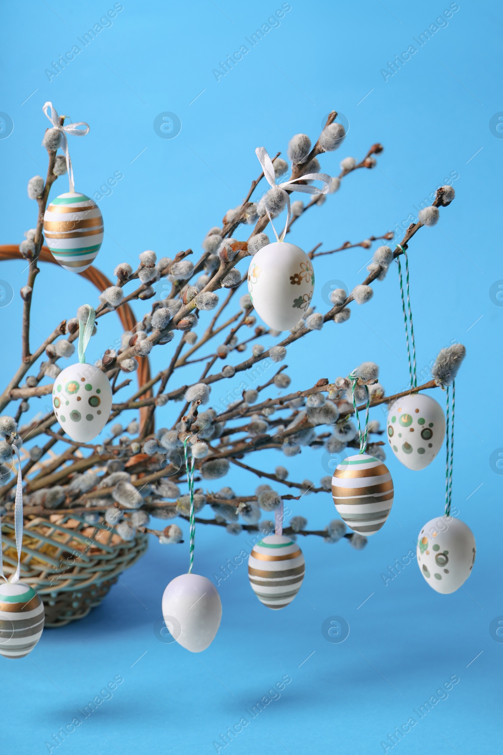 Photo of Wicker basket with beautiful willow branches and painted eggs on light blue background, closeup. Easter decor