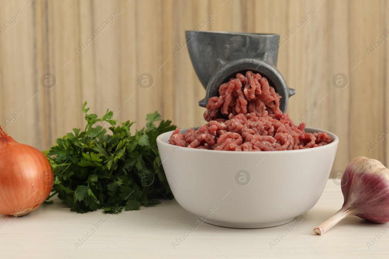 Photo of Mincing beef with manual meat grinder. Parsley, garlic and onion on white wooden table