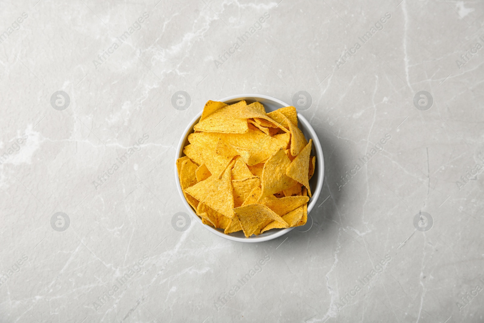 Photo of Tasty mexican nachos chips in bowl on grey table, top view