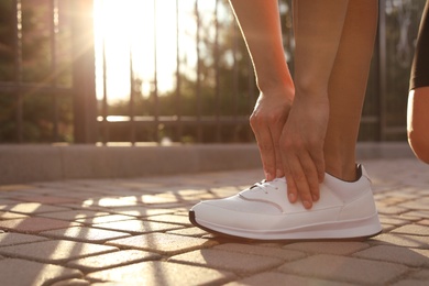 Young woman tying laces on street in morning, closeup. Space for text