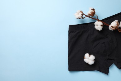 Photo of Black man's underwear and cotton flowers on light blue background, flat lay. Space for text