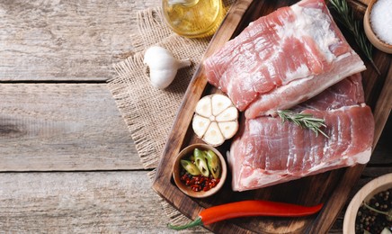 Photo of Pieces of raw pork belly, oil, garlic, salt and spices on wooden table, flat lay. Space for text