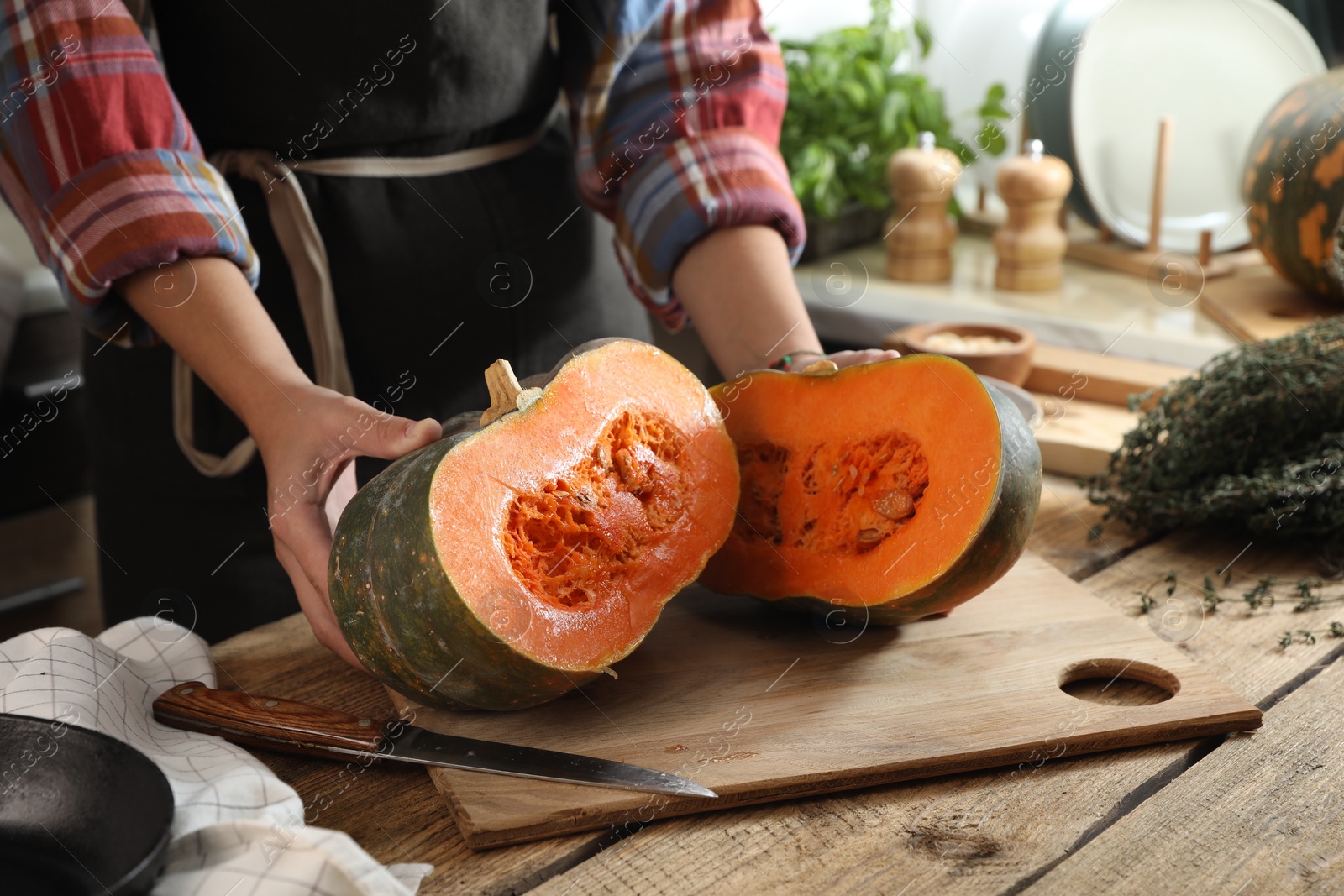 Photo of Woman with cut fresh ripe pumpkin at wooden table in kitchen, closeup