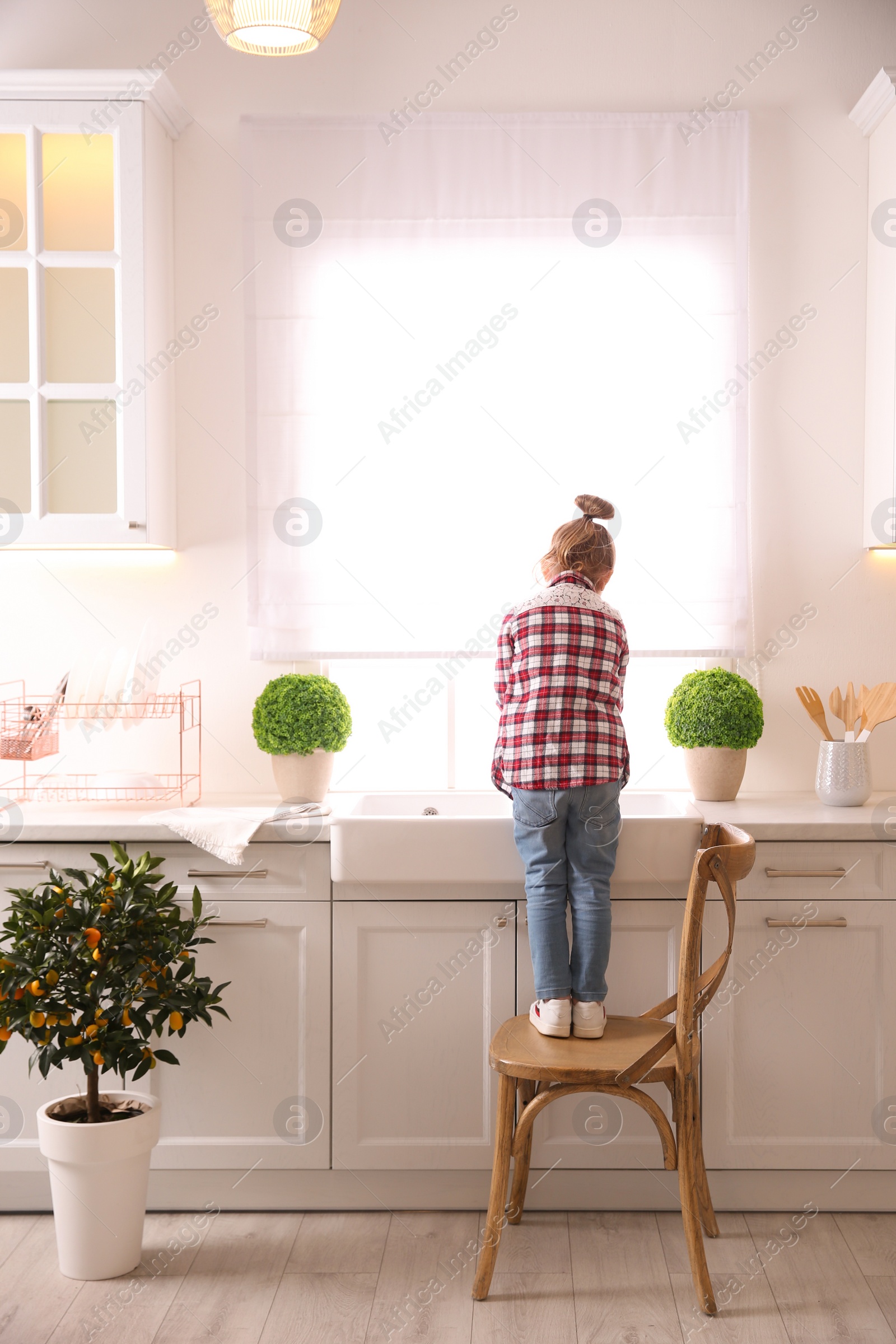 Photo of Little girl washing dishes in kitchen at home, back view