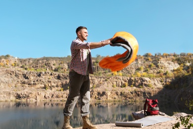 Young male camper with sleeping bag in wilderness