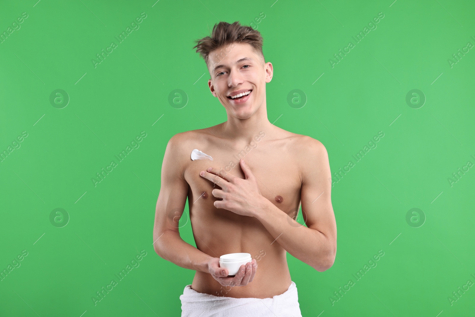 Photo of Handsome man applying moisturizing cream onto his shoulder on green background