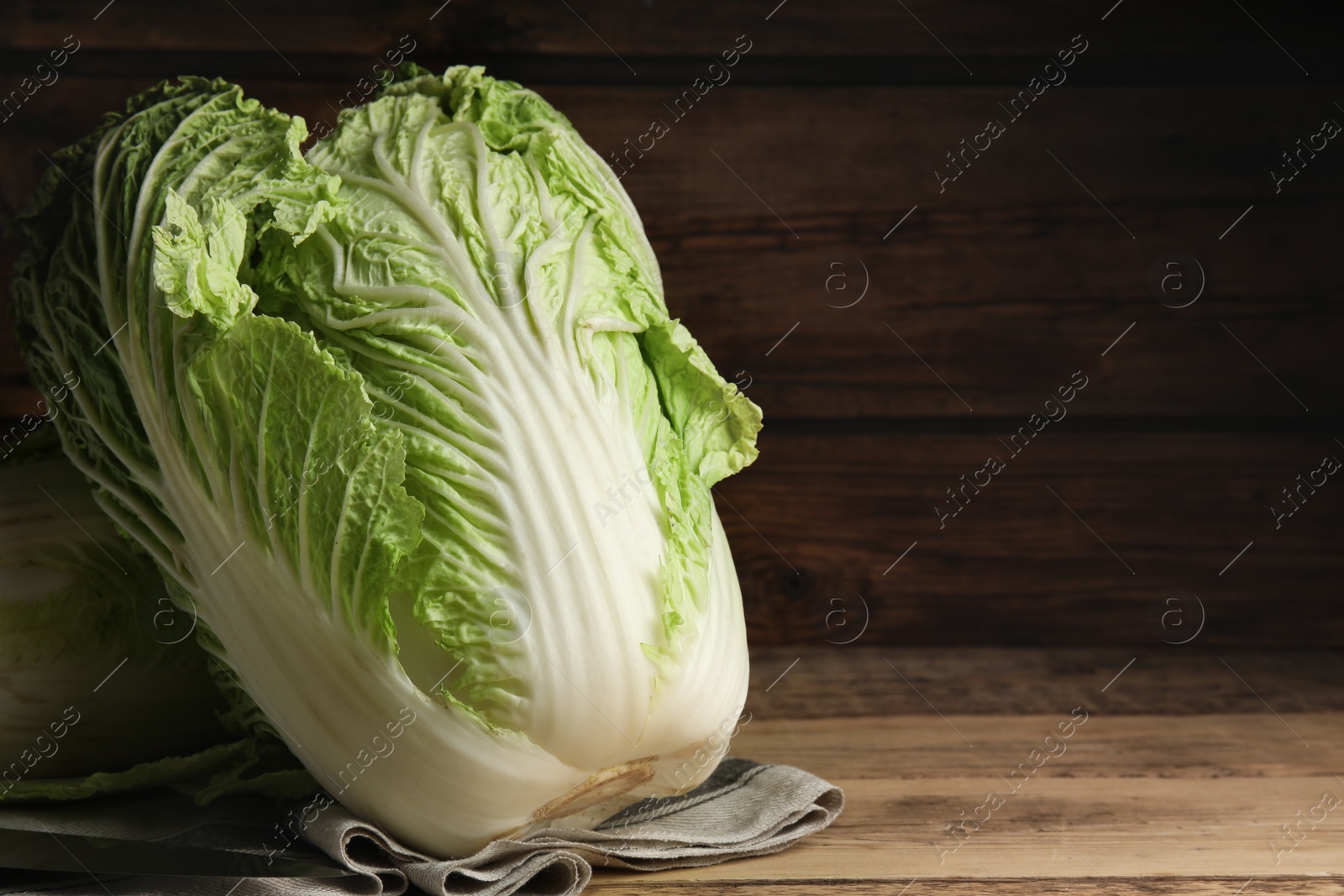 Photo of Fresh ripe Chinese cabbages and knife on wooden table, closeup. Space for text