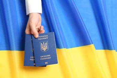 Woman holding Ukrainian travel passports over national flag, top view with space for text. International relationships