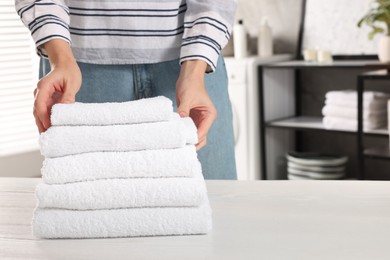 Photo of Woman stacking clean towels on white table in laundry room, closeup. Space for text