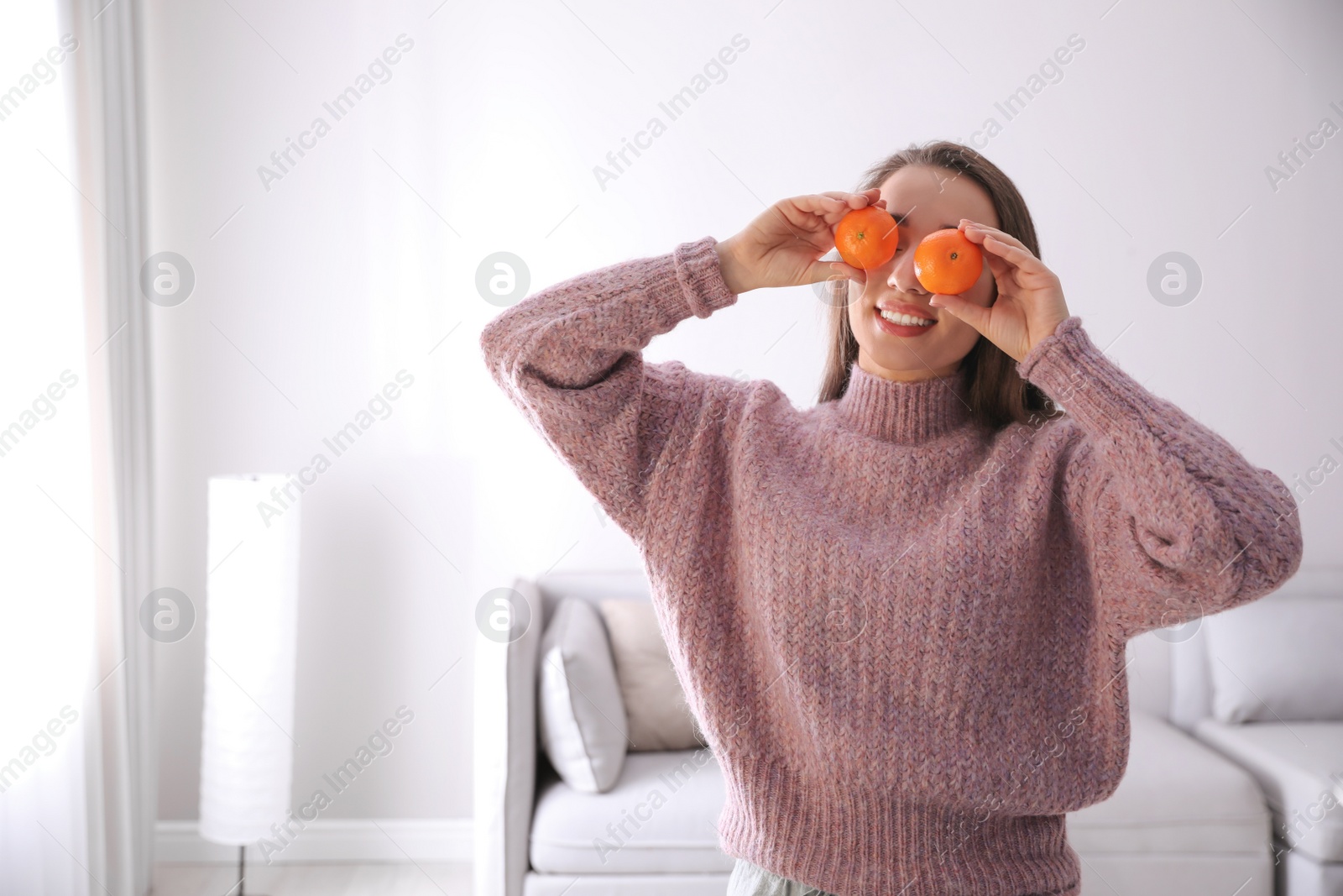 Photo of Happy young woman with fresh ripe tangerines at home