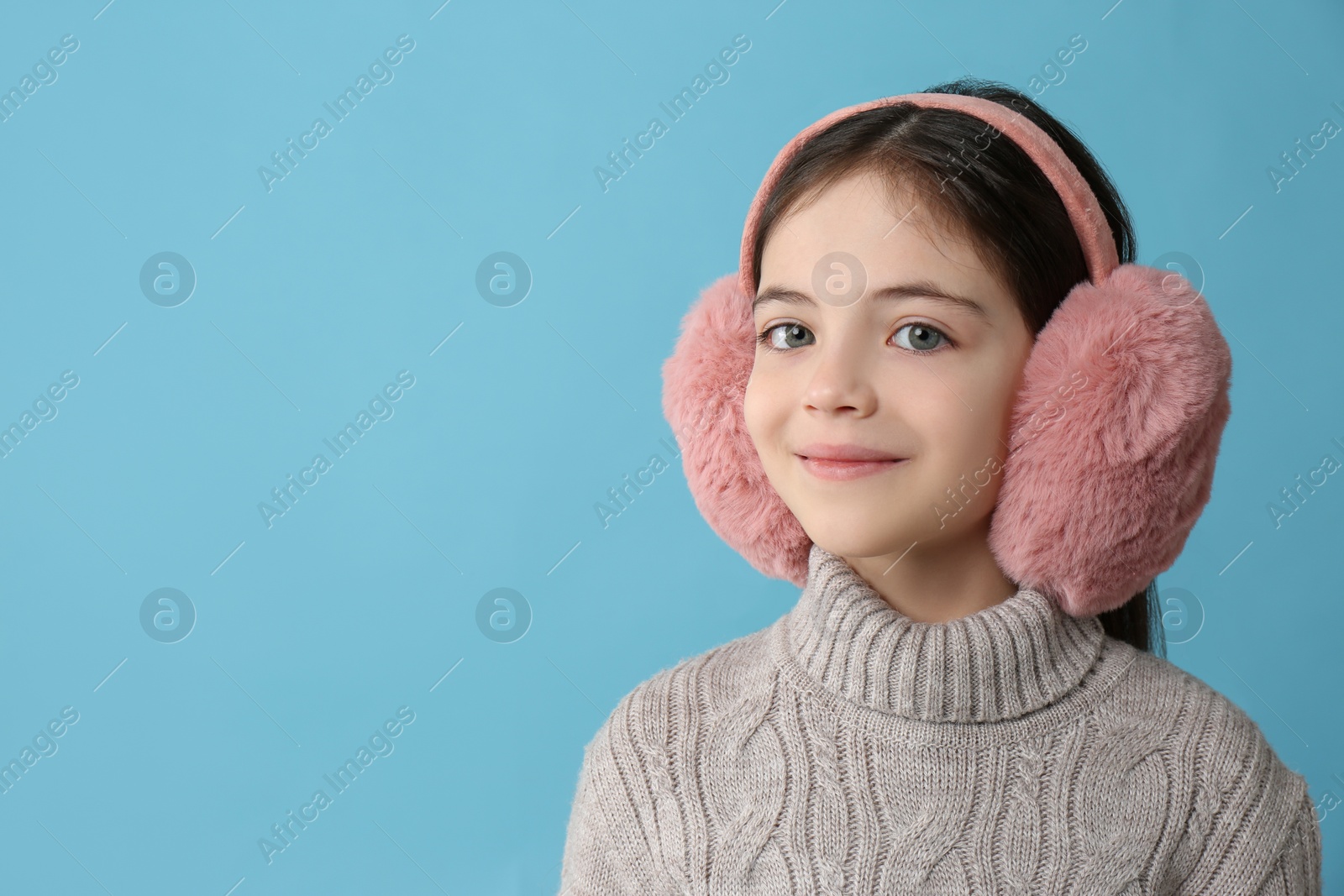 Photo of Cute little girl wearing stylish earmuffs on light blue background. Space for text