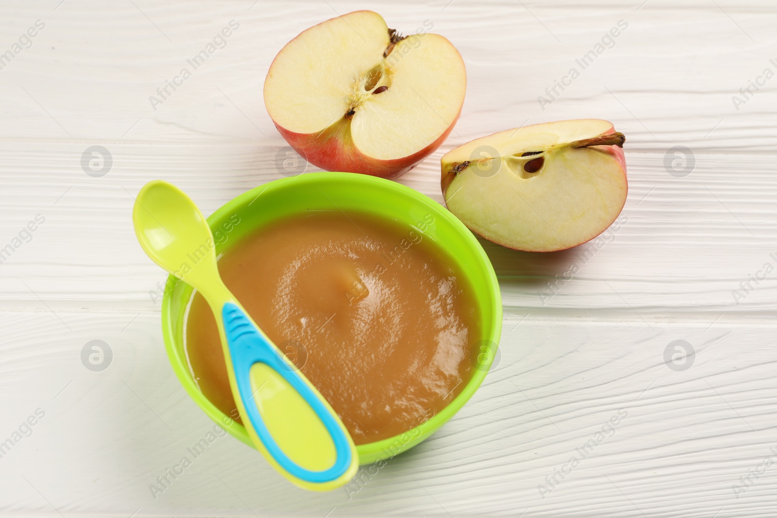 Photo of Baby food. Puree of apples in bowl and spoon on white wooden table