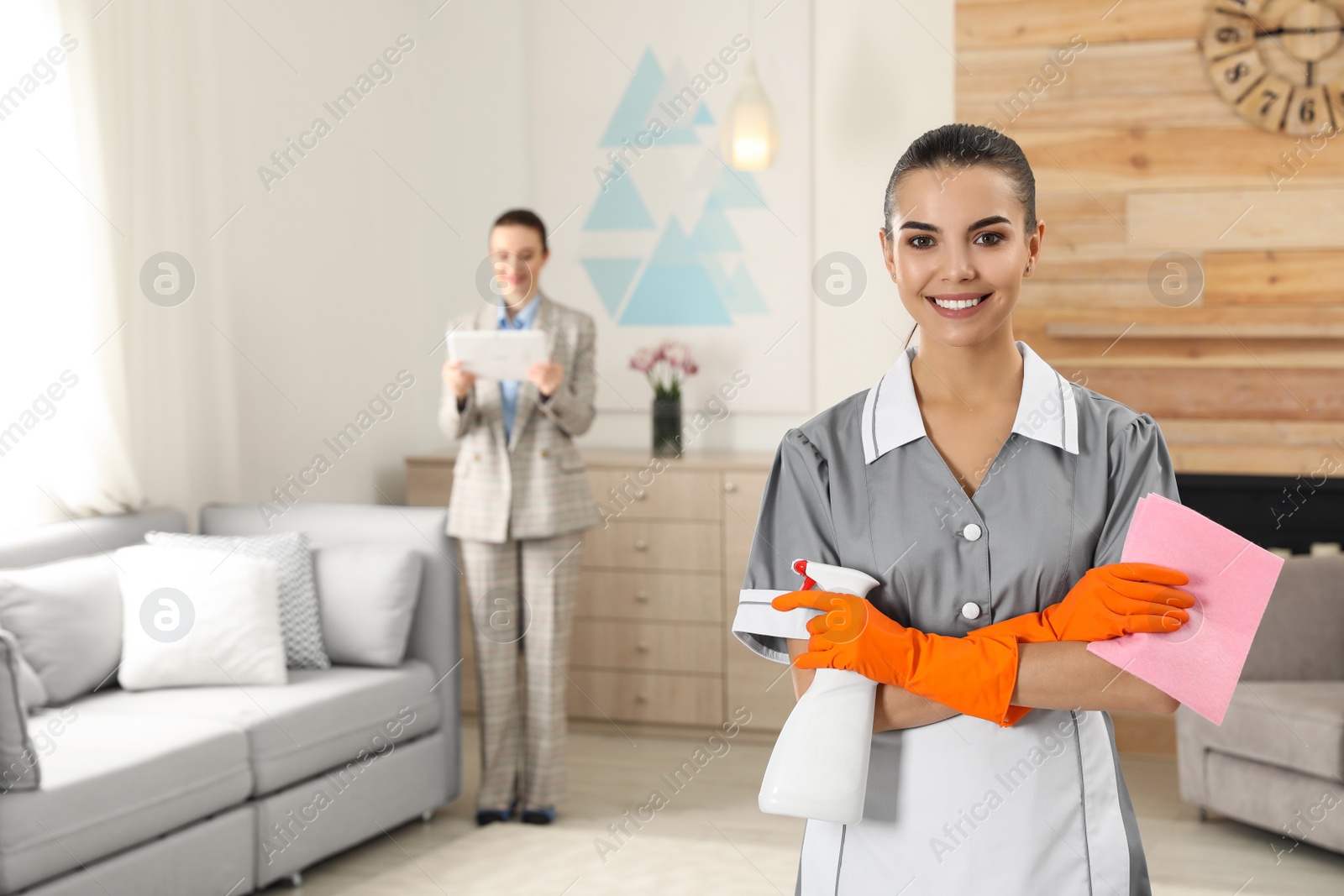 Photo of Portrait of young chambermaid and blurred supervisor in hotel room. Space for text