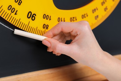 Photo of Woman drawing with chalk and protractor on blackboard, closeup