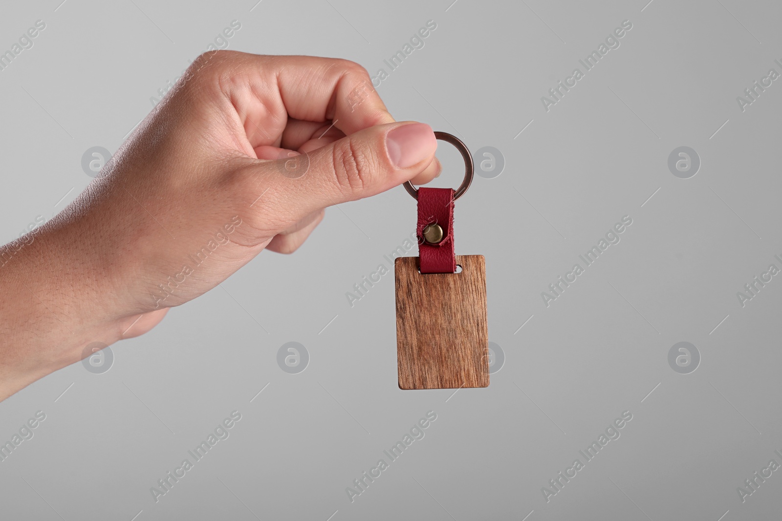 Photo of Woman holding wooden keychain on grey background, closeup