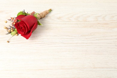 Stylish boutonniere with red rose on light wooden table, top view. Space for text