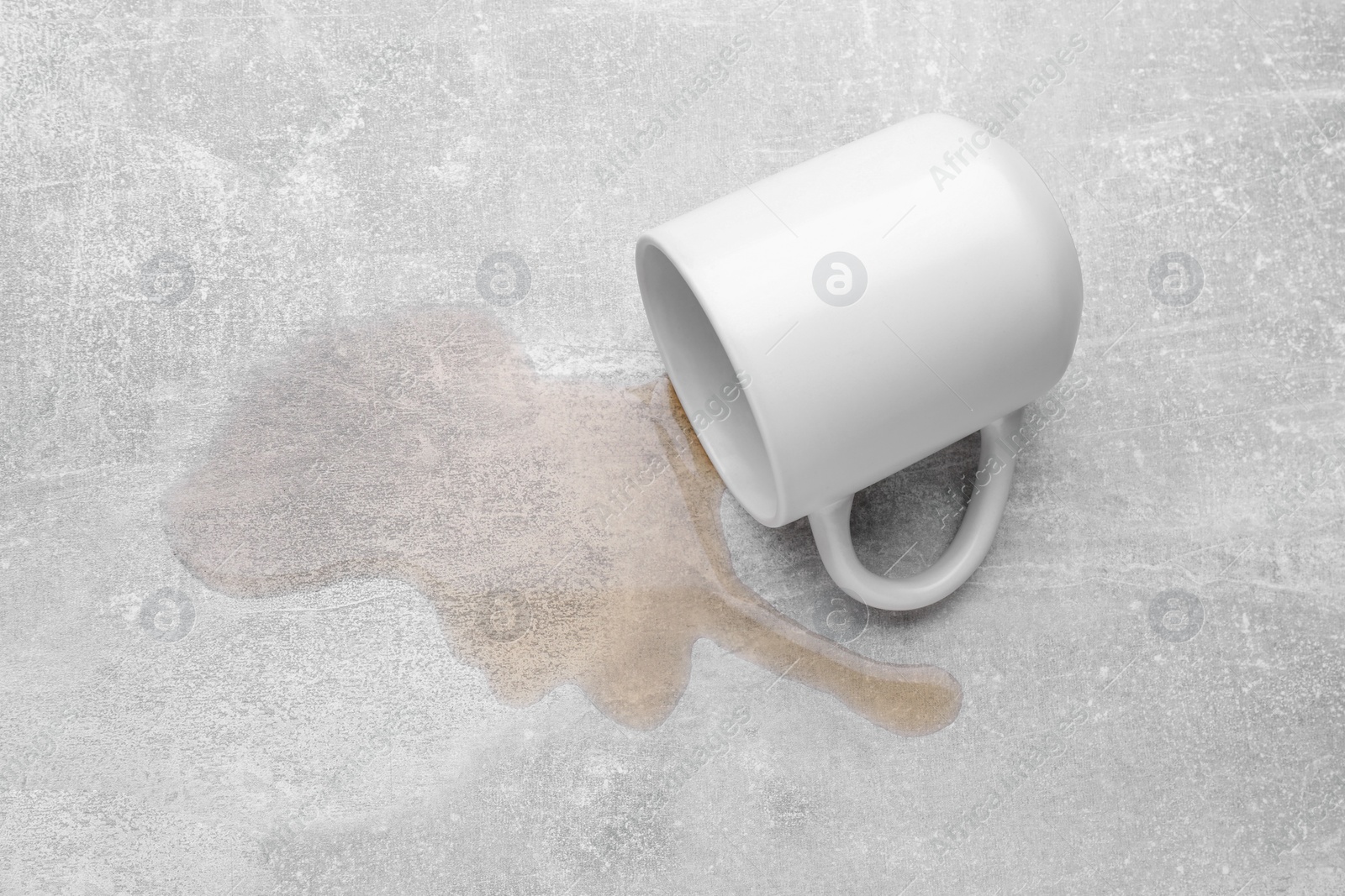 Photo of White mug with spilled liquid on light grey surface, above view