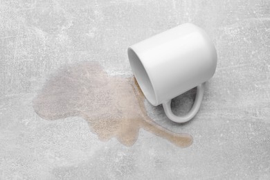 Photo of White mug with spilled liquid on light grey surface, above view