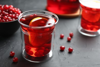 Photo of Tasty hot cranberry tea with lemon and fresh berries in glass on black textured table