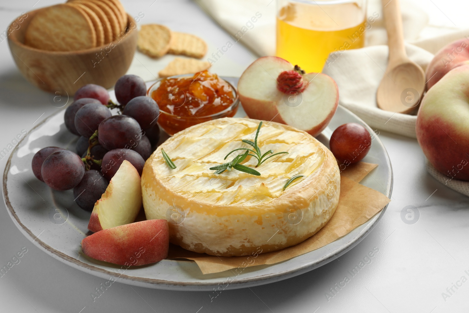 Photo of Tasty baked brie cheese with fruits and jam on white marble table, closeup