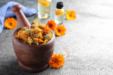 Photo of Wooden mortar with dry calendula flowers on light grey table. Space for text