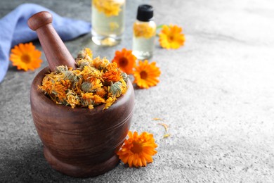 Wooden mortar with dry calendula flowers on light grey table. Space for text