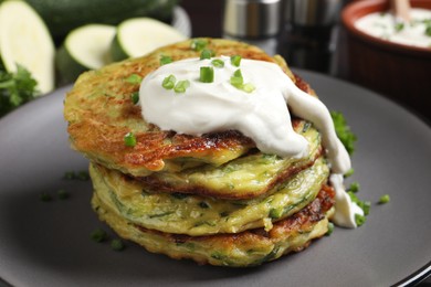 Delicious zucchini fritters with sour cream on plate, closeup view