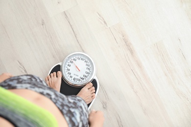 Photo of Woman measuring her weight using scales on wooden floor, top view. Healthy diet
