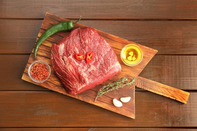 Photo of Fresh raw beef cut, spices and oil on wooden table, top view