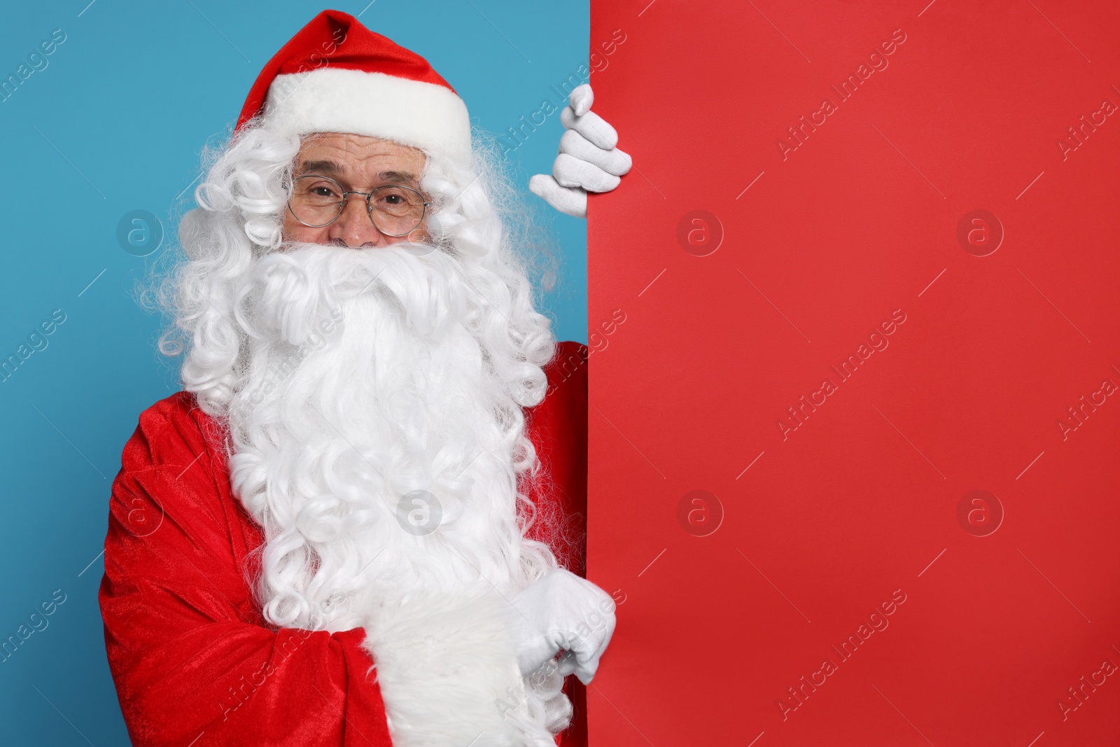 Photo of Santa Claus holding blank red poster on light blue background, space for text