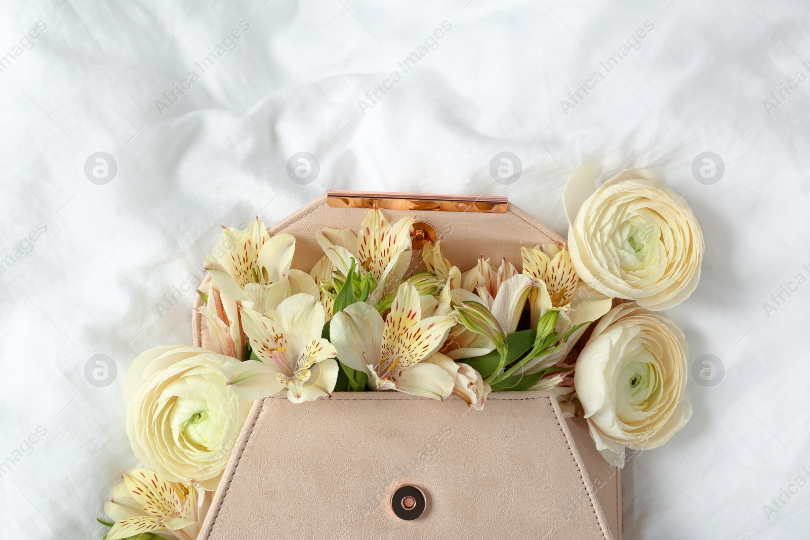 Photo of Stylish clutch with spring flowers on crumpled sheet, top view