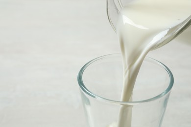 Photo of Pouring milk into glass on white table, closeup. Space for text