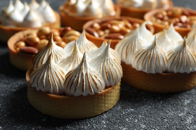 Photo of Many different tartlets on black textured table, closeup. Tasty dessert