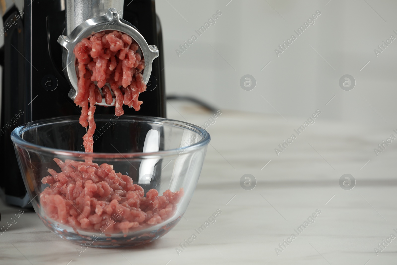 Photo of Electric meat grinder with beef mince on white table against blurred background, closeup. Space for text